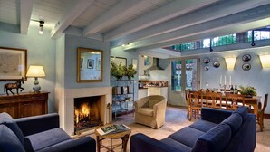A spacious living room with a fireplace, comfortable seating, a dining area, and a kitchen visible through an open door.