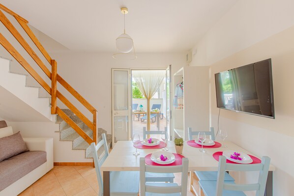 A dining area with a table set for four, a wooden staircase, and a TV mounted on the wall.