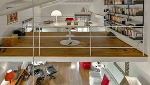 A modern interior with a wooden floor, a round table with a white lamp, a red chair, a bookshelf, and a red bean bag.