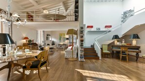 A spacious living area with a dining table, chairs, a piano, and a staircase leading to an upper level.