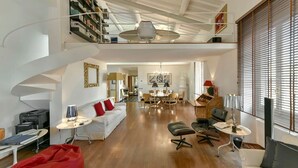 A spacious living area with a staircase, a dining area, and a seating area with a red bean bag.