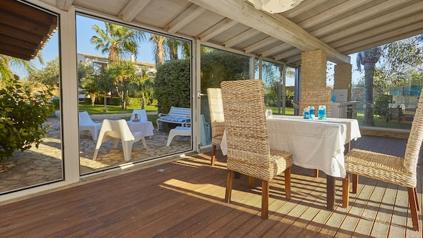 An outdoor patio with wicker chairs and a table, large glass doors, and a view of a garden and palm trees. - Villa with splendid pool near the beaches, 4 bedrooms (Marinella di Selinunte)