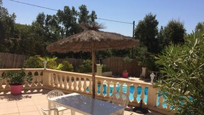 Un patio al aire libre con una mesa y sillas, un toldo de paja, una piscina y una valla de madera.