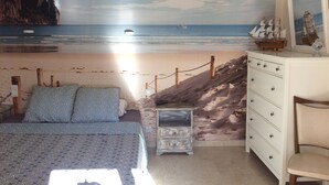 Un dormitorio con un mural de playa, una cama con ropa de cama estampada, un aparador y una silla.