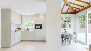 Une cuisine moderne dotée d’appareils électroménagers intégrés, un coin repas avec une table et des chaises, et une grande porte-fenêtre coulissante donnant sur un espace extérieur.
