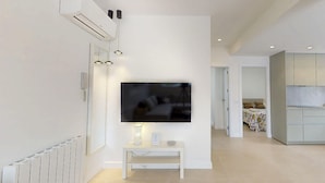 Un salon moderne avec un téléviseur à écran plat fixé au mur, une console blanche agrémentée d’objets décoratifs et un radiateur également fixé au mur.