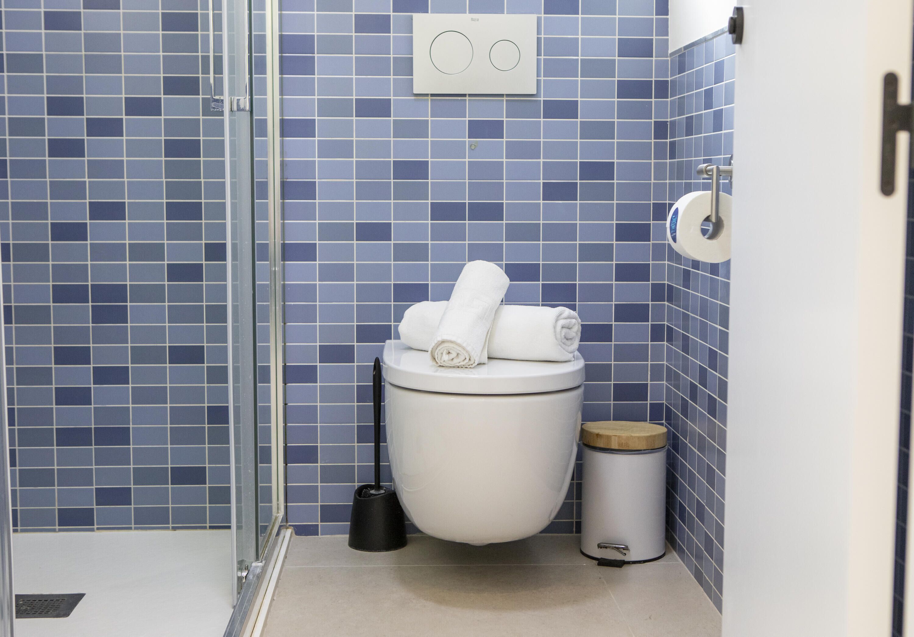 Ein Badezimmer mit Toilette, Mülleimer, Handtrockner und Duschbereich.