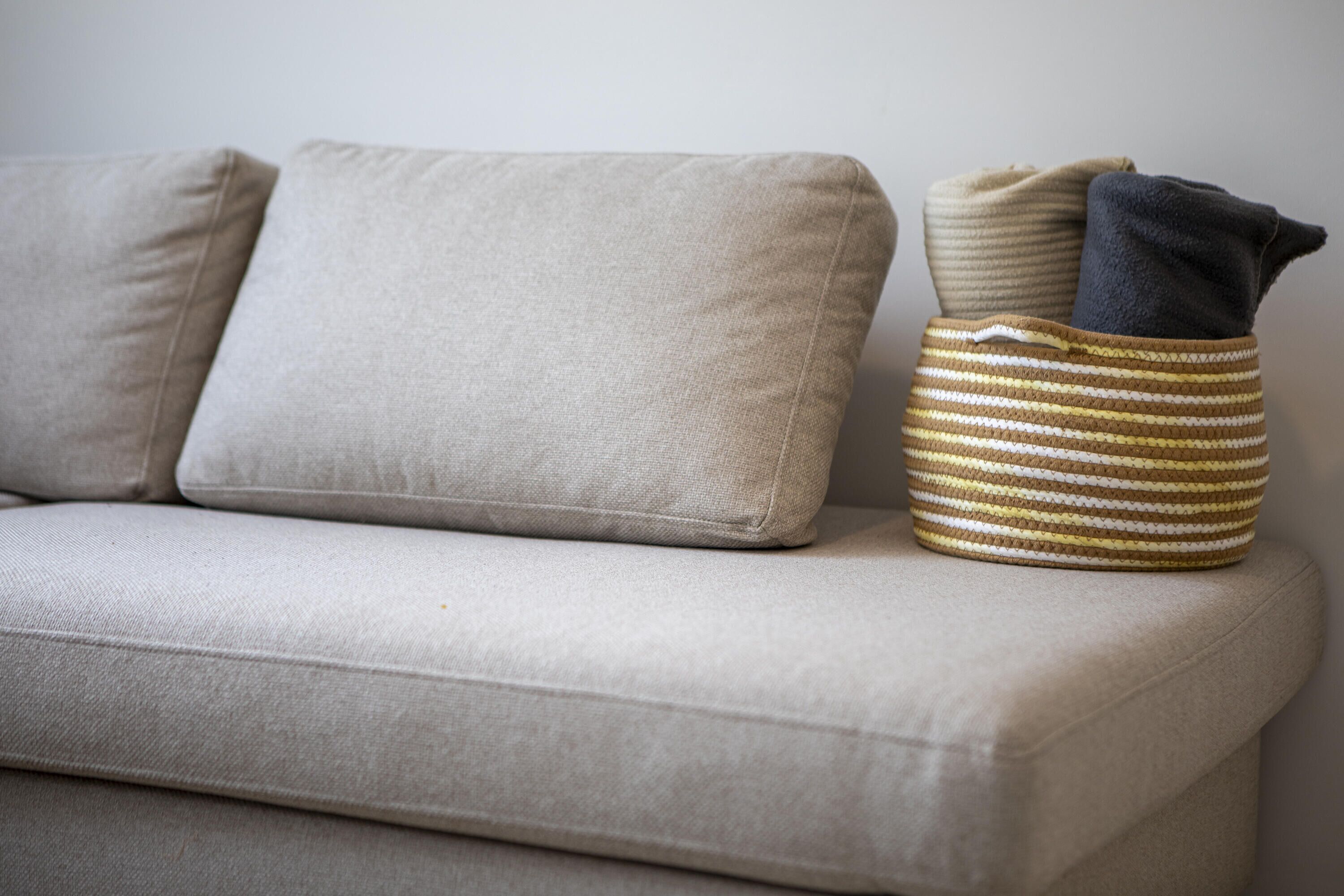 A sofa with two cushions and a striped basket with folded items.