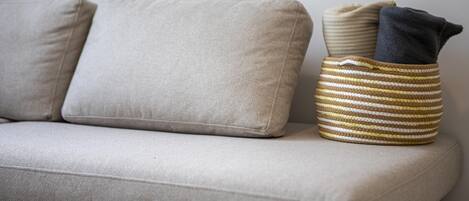 A sofa with two cushions and a striped basket with folded items.