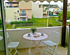A balcony with two white striped chairs and a small round table, overlooking a residential area with houses and a green lawn.