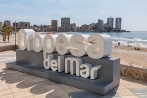 A large, modern sign with the text "Oropesa del Mar" in a bold, sans-serif font, set against a backdrop of a beach and city skyline.