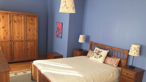Een slaapkamer met een houten bed, twee nachtkastjes, een houten garderobe en een blauwe wand.