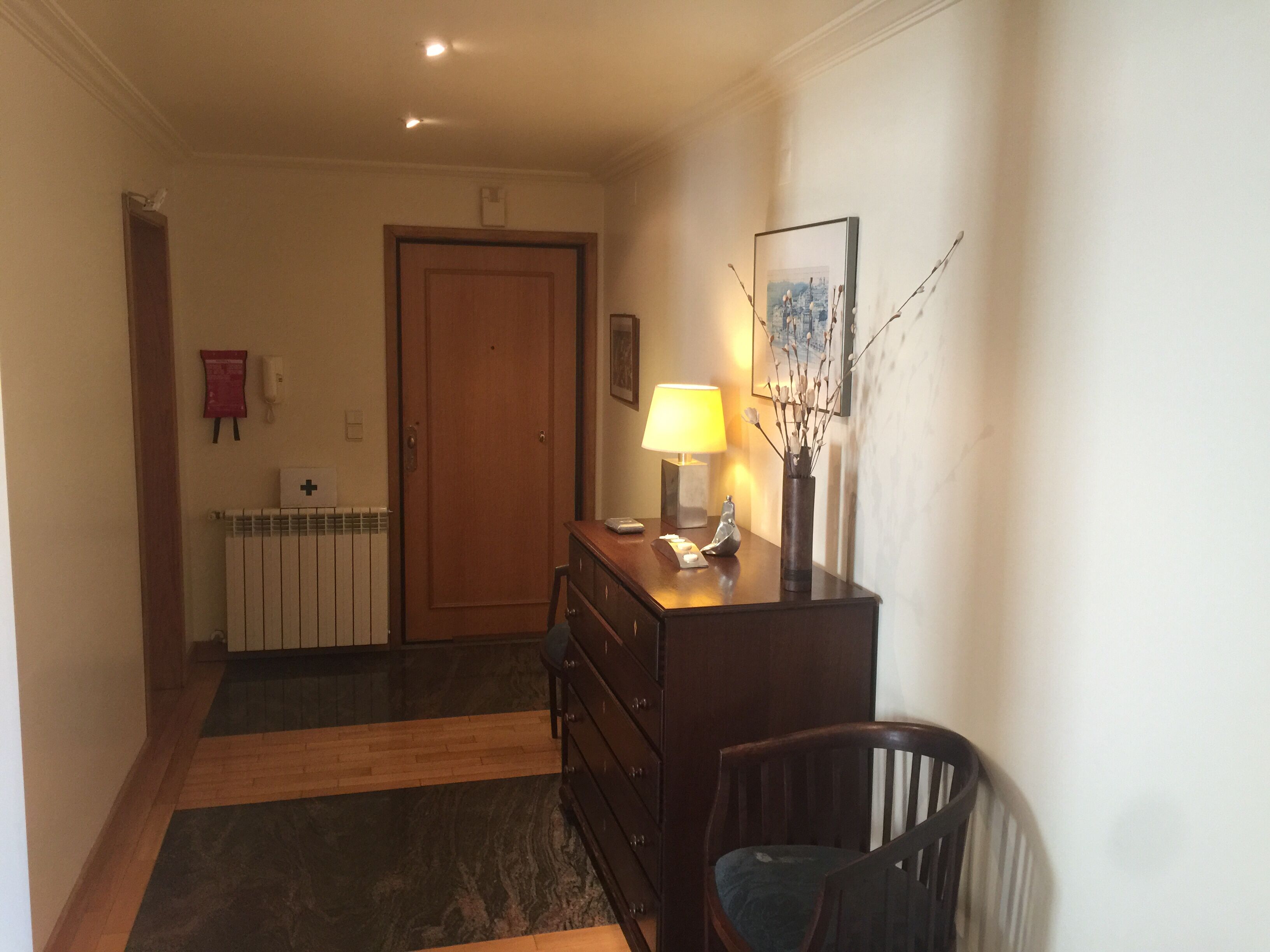A hallway with a wooden door, a radiator, a desk with a lamp, and a chair.