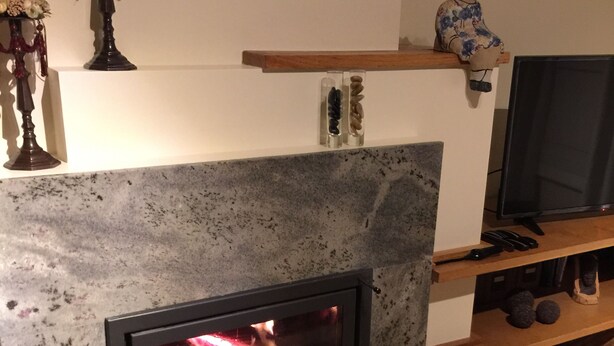 Een moderne haard met een stenen gevel, een houten plank erboven en een televisie op een standaard aan de rechterkant.