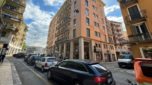A multi-story building with balconies, a parking lot with several cars, and a clear sky.