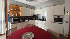 A compact kitchen with white cabinets, a microwave, stove, and a dining table with a red tablecloth.