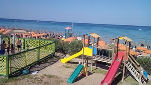 Ein Strand mit einem Spielplatz, darunter Rutschen und einem eingezäunten Bereich.