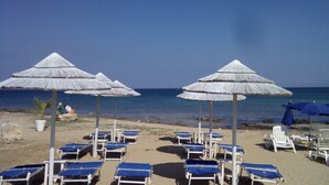 Ein Strand mit Liegestühlen und strohgedeckten Sonnenschirmen.