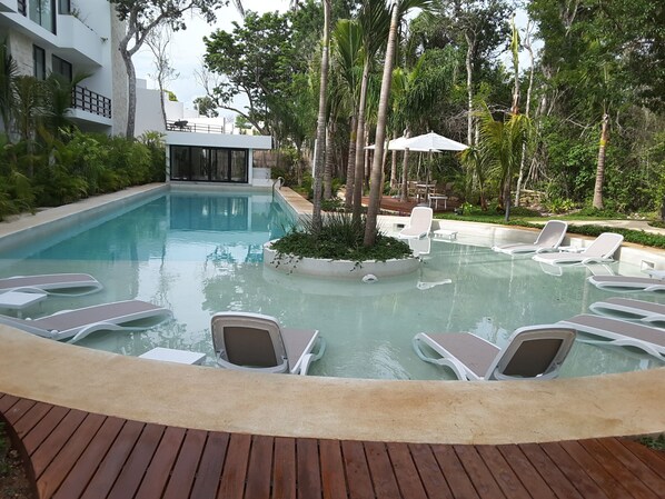 A pool area with lounge chairs, a wooden deck, and a building in the background.