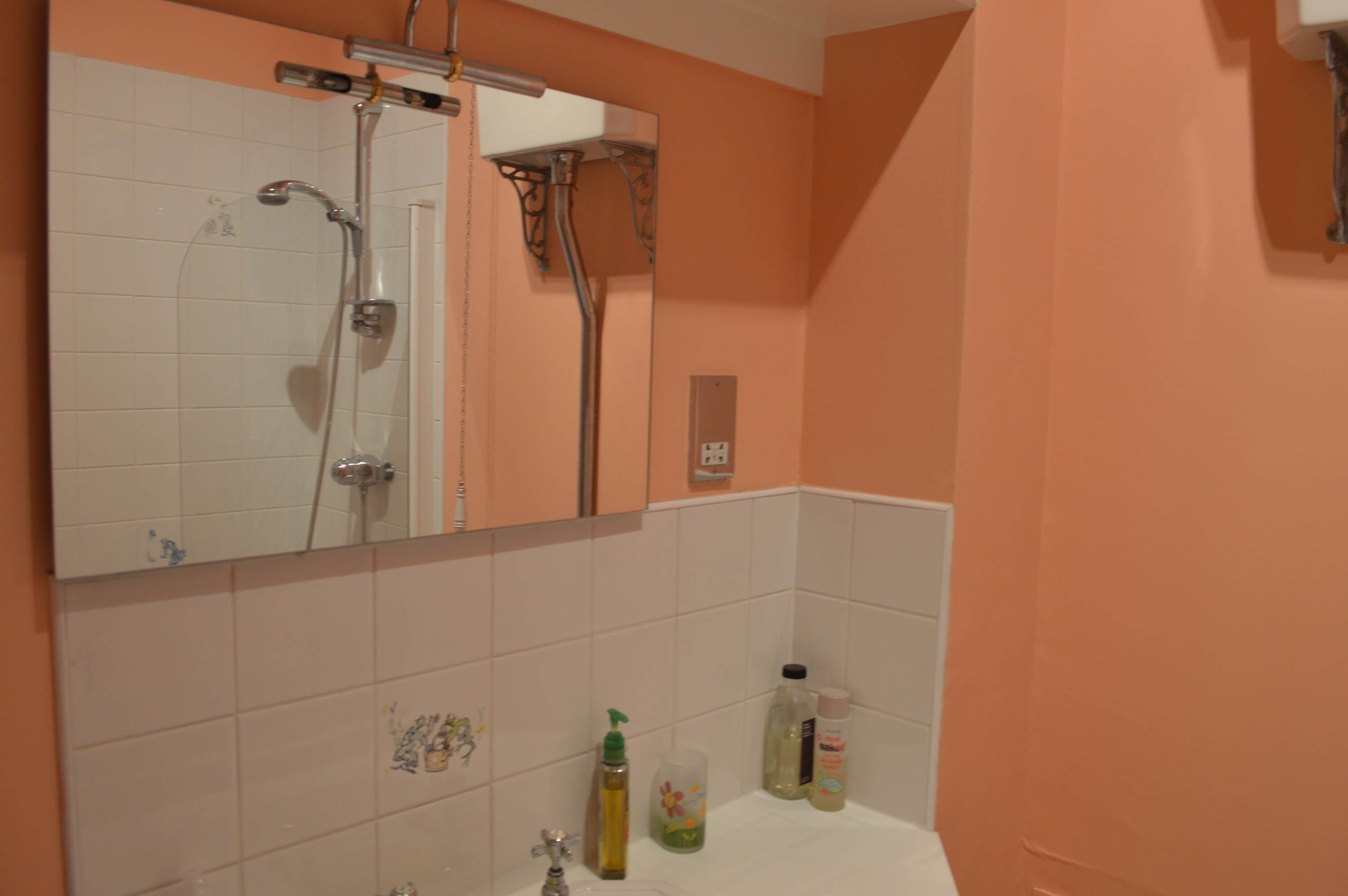 A bathroom with a large mirror, white tiles, a shower, and a sink with toiletries.