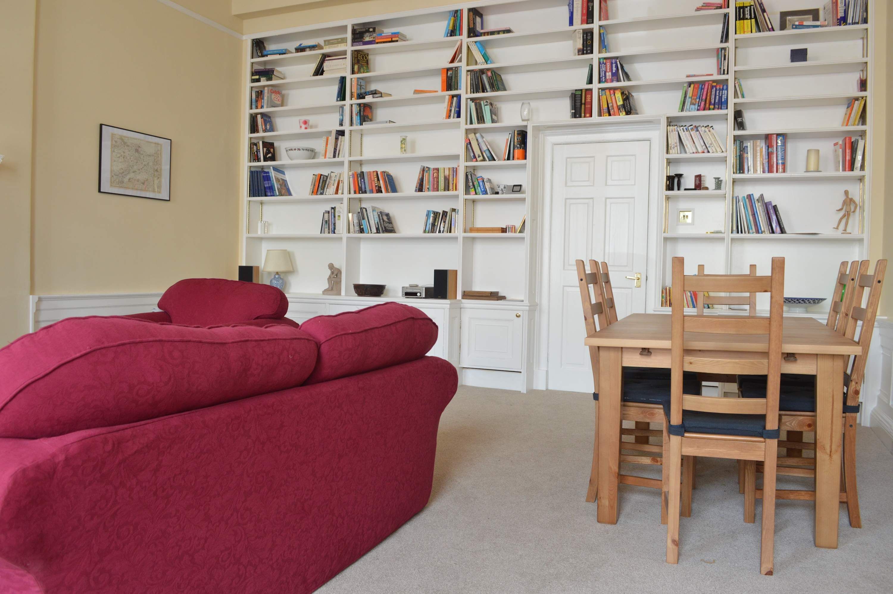 A room with a red sofa, a wooden dining table with chairs, and a bookshelf filled with books.