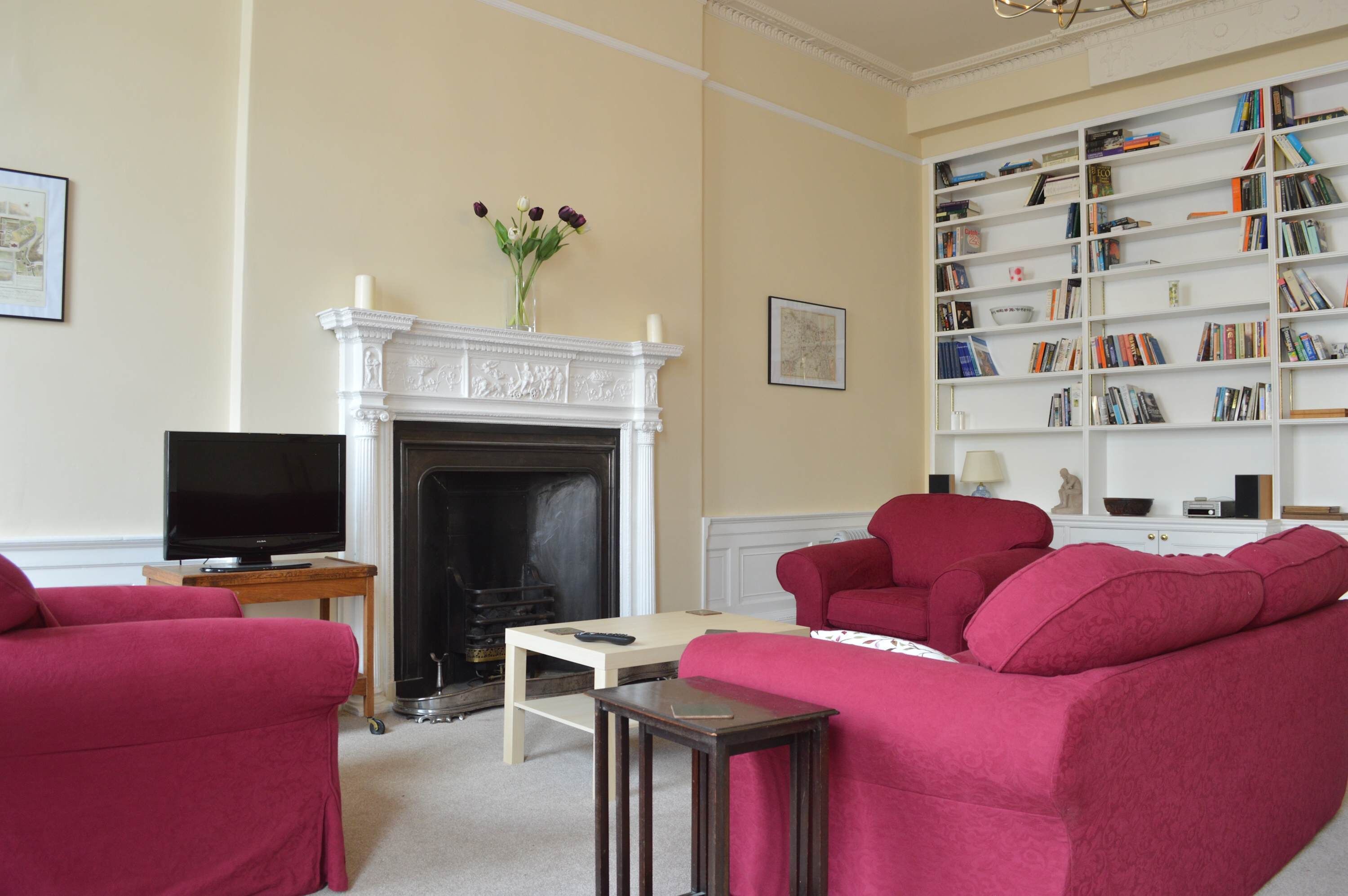 Ein Wohnzimmer mit Kamin, Fernseher, Bücherregal und zwei roten Sofas.