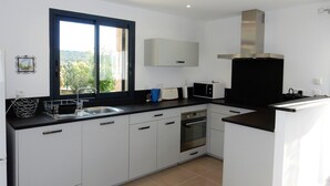 A modern kitchen with white cabinets, a black countertop, a built-in oven, and a window with a view of greenery. - Superb villa in Porto-vecchio  (Porto-Vecchio)