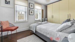 A bedroom with a bed, a chair, a wardrobe, and windows with blinds.