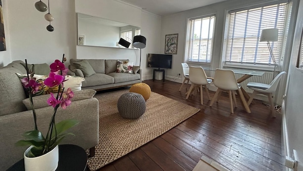 A modern living room with a grey sofa, a coffee table, and a TV. There are two chairs and a small table with a lamp.