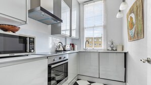 A modern kitchen with white cabinetry, a black and white checkered floor, a microwave, an oven, and a window with blinds.