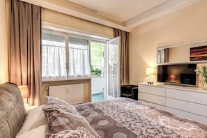 A bedroom with a bed, a dresser, a TV, and a window with curtains.