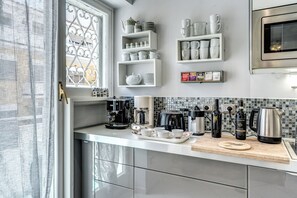 A modern kitchen with white cabinetry, a coffee station, and a decorative window.