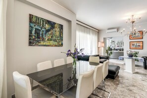 A modern living room with a dining area, a chandelier, and artwork on the walls.