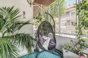 A hanging chair with cushions, a potted plant, and a tiled floor.