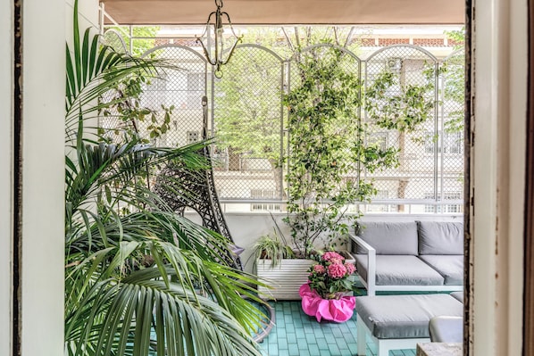 A balcony with a white sofa, a pink flower pot, and a metal fence.