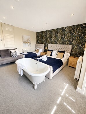 A bedroom with a large bed, a smaller bed, a bathtub, a sofa, and a radiator. - Cozy converted stable -Room 1 (york)