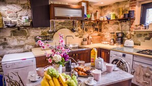 Una cocina con paredes de piedra, un lavamanos, una cafetera y una zona de comedor con una mesa dispuesta para el desayuno.