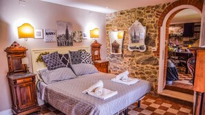 Un dormitorio ordenado con suelo a cuadros, una cama grande con ropa de cama estampada, dos mesitas de noche con lámparas y una pared de piedra.