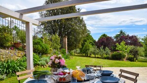 Un área de comedor al aire libre con una mesa preparada para cuatro personas, rodeada de abundante follaje y un muro de piedra.