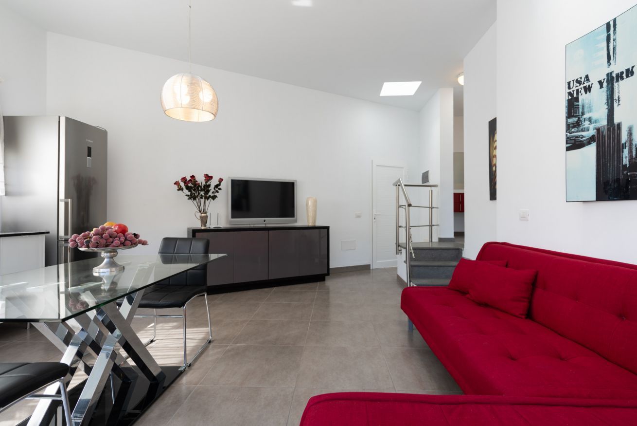 Un espace de vie moderne comprenant une table à manger en verre, un canapé rouge, un téléviseur et un escalier.