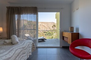 A hotel room with a bed, a red chair, a small table, and a view of a hillside. - Holidays & Health in Finca Oasis - Villa 7 by Viilas Rivero (Telde)