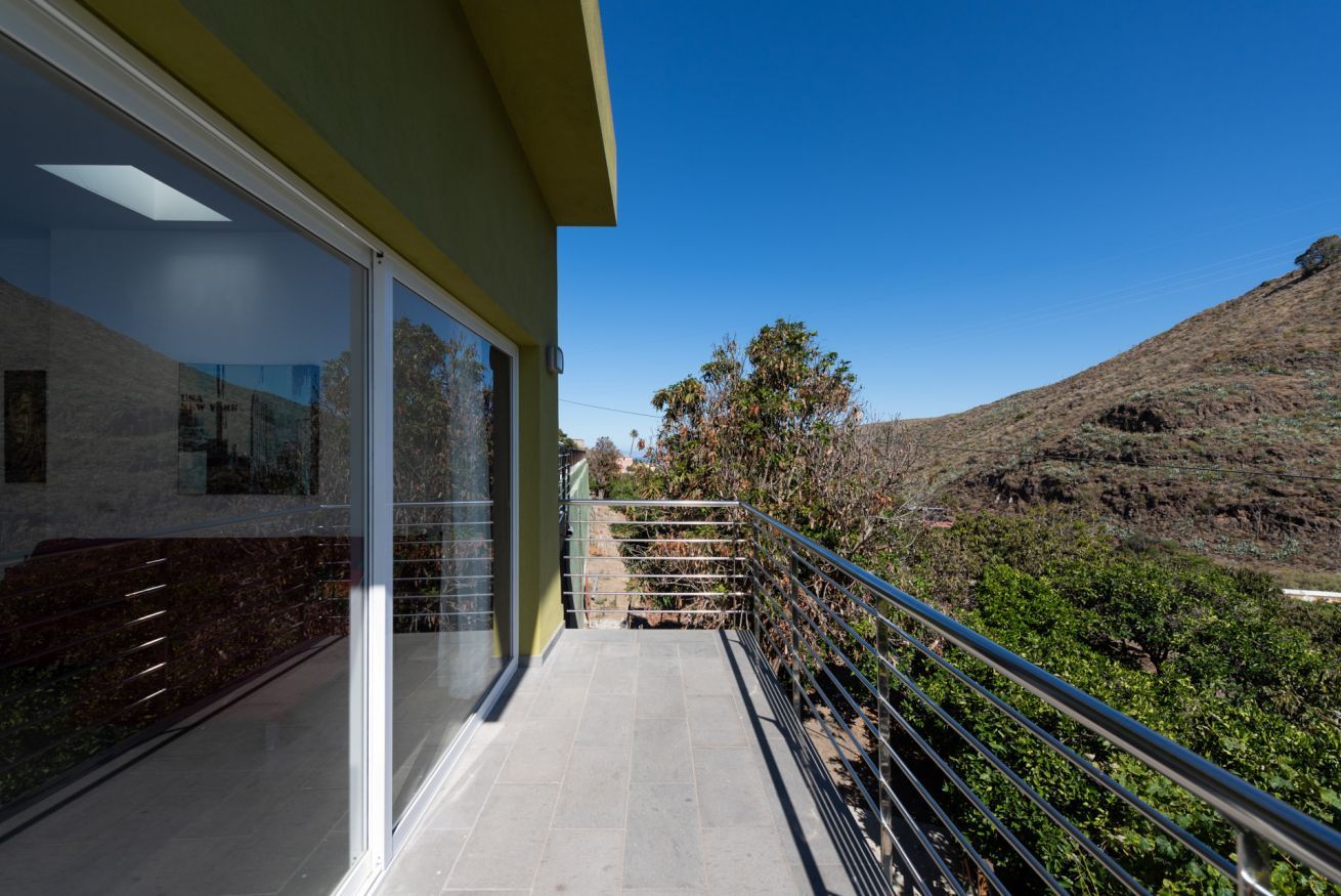 A balcony with a metal railing, a clear sky, and a hilly landscape in the background.