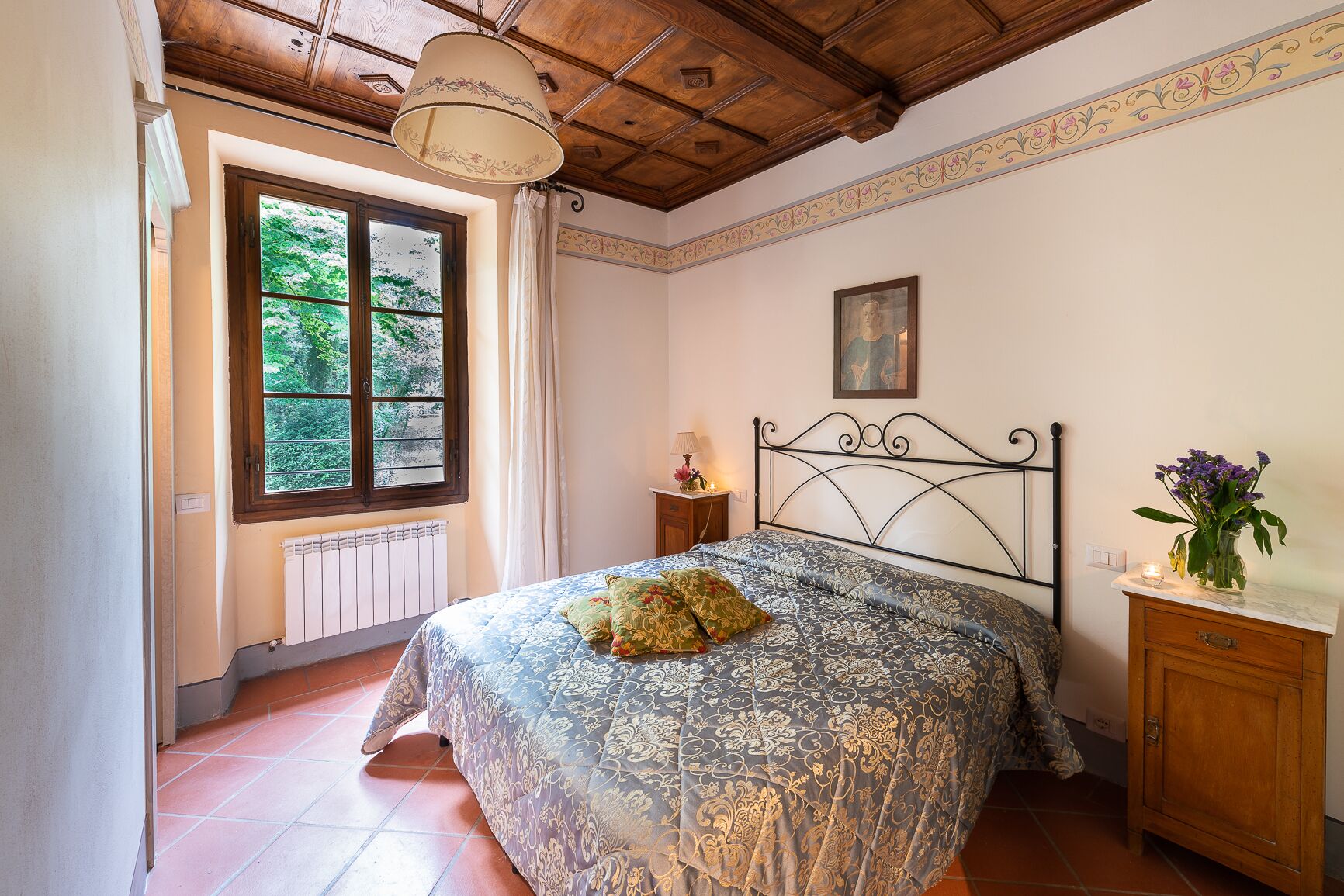 Un dormitorio con cama, mesita de noche, ventana, radiador y un armario de madera.