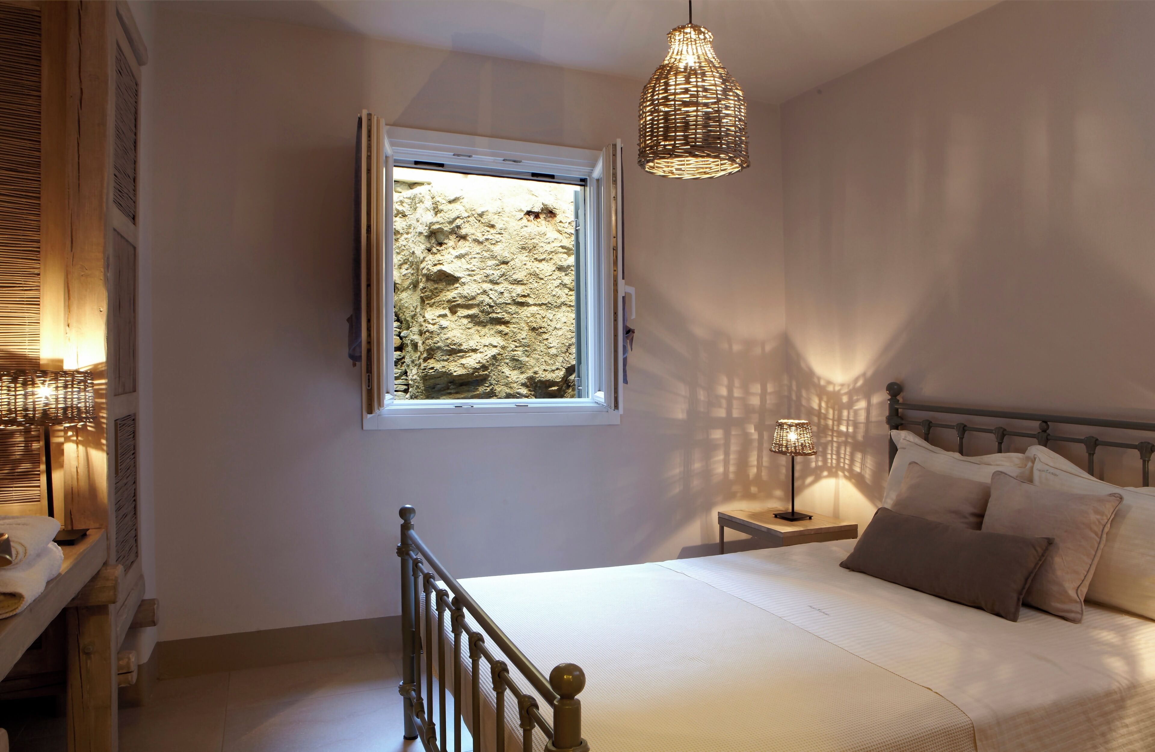 Un dormitorio con cama, mesita de noche, lámpara y ventana con vistas a un paisaje rocoso.