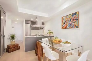 A modern kitchen with a central island, white chairs, a glass dining table, and a colorful abstract painting on the wall. - BARCELONA DOWNTOWN! (Barcelona)