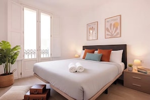 A neatly made bed with rolled towels, a bedside table with a lamp, and two framed artworks on the wall.