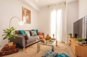 Un salon moderne avec un canapé, une table basse en verre, un téléviseur et une grande fenêtre avec des rideaux.