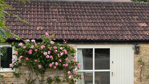 Ein Haus aus Stein mit Ziegeldach, einer weißen Tür und Kletterrosen, die die Wand hinaufwachsen.