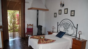 Un dormitorio con una cama, una silla, una mesita de noche, una lámpara y un estante en la pared.