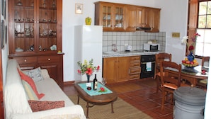 Una sala de estar con un sofá, una mesa de centro con un florero y una botella de vino, y una cocina con armarios de madera y un salpicadero de azulejos.